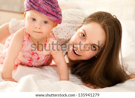happy-looking baby wearing knitting hat and  beautiful mother playing together on the bed