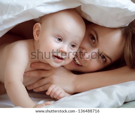 happy-looking baby and  beautiful mother playing together on the bed