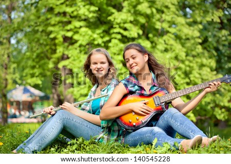 two girls playing guitar and flute in the park