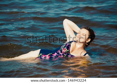 Happy young plus size woman in swim suite laying on sea shore