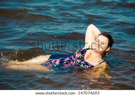 Happy young plus size woman in swim suite laying on sea shore