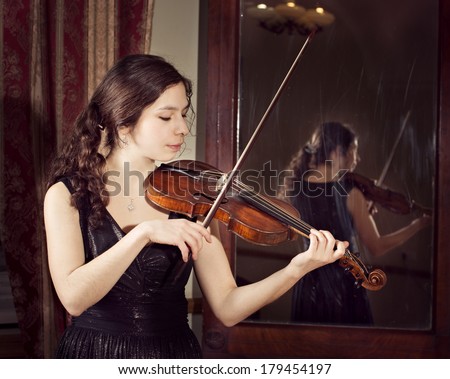 beautiful young happy woman play  baroque violin. Antique mirror as background
