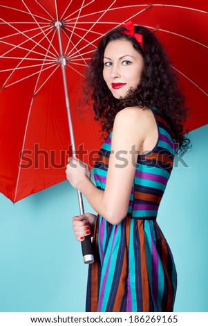Brunette pin up model posing wearing striped dress posing with red umbrella