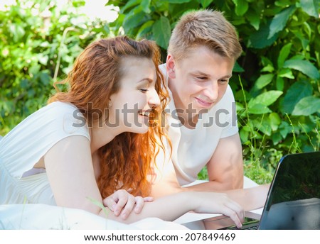 young couple have dating in the park. Computer. Red haired curly girl