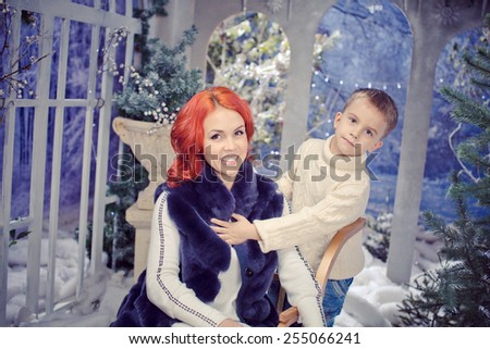 red headed mother and  son  playing.  Winter landscape. Woman wearing fur vest. son wearing white knittiing sweater