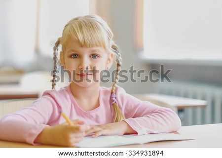 Cute five years old  blonde girl sitting at classroom and writing