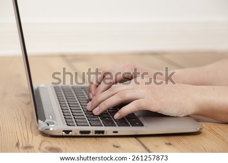woman typing on laptop on wooden floor