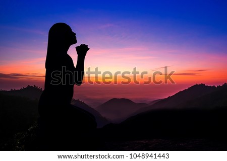 Silhouette of woman kneeling and praying over beautiful sunrise