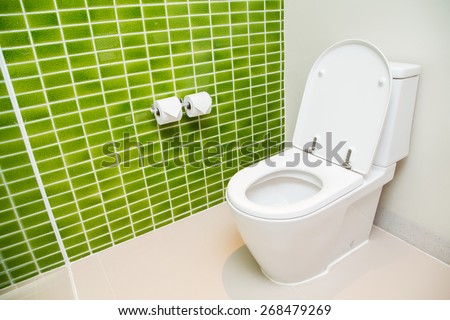 Clean, white toilet and paper rolls with Lime green mosaic tiles wall