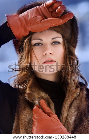 Young beautiful woman in fur hat and brown gloves at winter forest