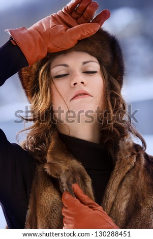 Young beautiful woman in fur hat and brown gloves at winter forest close eyes