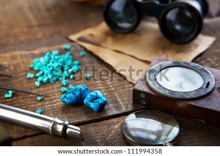 Treasure hunting, or gem stone hunting. A compass, magnifying glasses and turquoise stones on a old wood desk.