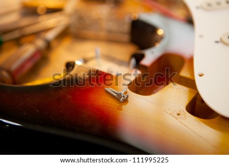 Guitar on guitar repair desk. Electric guitar on a guitar repair work shop. Neck and pickguard detached. Double cutaway solid body guitar, sunburst color. Shallow depth of field.