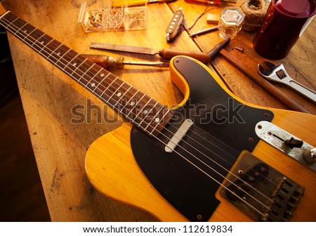 Guitar on guitar repair desk. Vintage electric guitar on a guitar repair  work shop. Single cutaway solid body guitar, amber color. Warm lighting