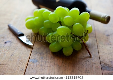 white grapes on a old wooden table with an old fruit knife and wine bottle in background.