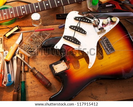 Sunburst electric guitar on guitar repair desk or in a repair work shop. Neck and pickguard detached. Double cutaway solid body guitar. Shallow depth of field.