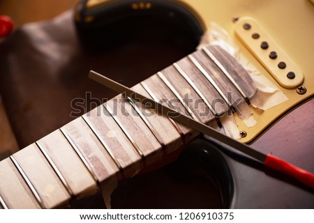 Refretting an electric. Electric guitar in  a guitar repair shop with file on fret. Double cutaway solid body guitar.