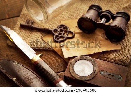 Treasure hunting setting, A compass, binoculars, knife and a old key on a old wooden desk