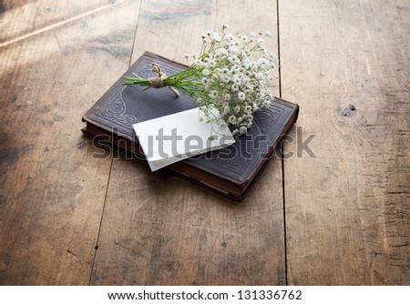 Vintage book and a small bouquet of baby\'s breath flowers and a blank sheet of folded white memo paper, on a well used old desk or wooden surface.