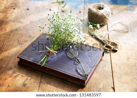 Vintage book, vintage eyeglasses and small bouquet of baby\'s breath flowers on old worn desk, in warm sunlight by the window.