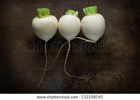 Three white radishes with long center root still intact, on a old wooden table with artistic feeling.