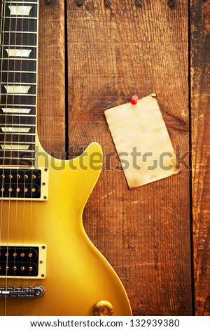 Vintage gold top single cutaway guitar on old wood surface and blank piece of paper, good for playlists, and production notes.