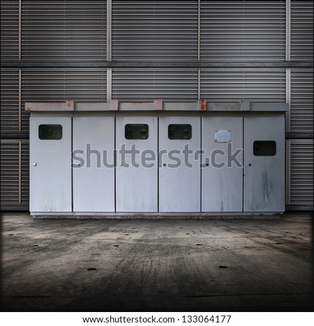 Electric utility boxes in a facility. Facility or Base type of grungy interior, with metal siding wall and concrete floor.