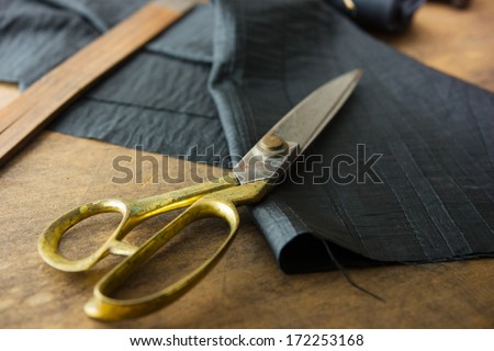 Measuring and cutting textile or fine cloth. Work table of a tailor. Gold scissors and black fabric.