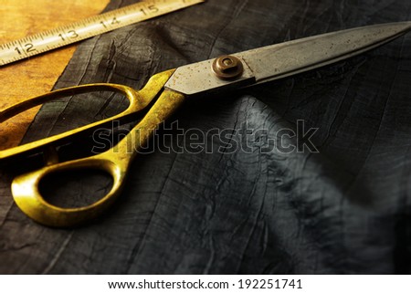Measuring and cutting textile or fine fabric. Work table of a tailor. Gold scissors and black fabric.