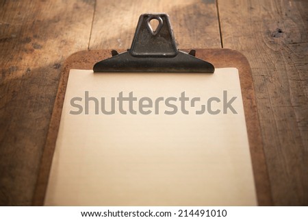 An vintage clipboard on a old wooden table, with blank old white paper.  Focus is on the writing area.