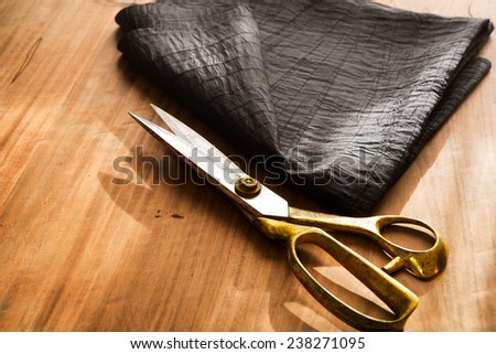 Tailor\'s work table. textile or fine cloth making.Gold scissors and black silky fabric.