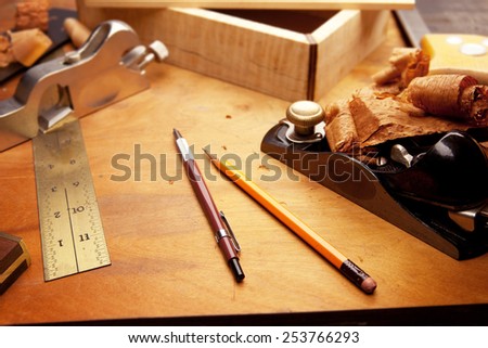 Fine wood working. Saw, hand plane, pencils and a wooden shavings on a work desk under incandescent light.Focus is on forehand side of two pens.