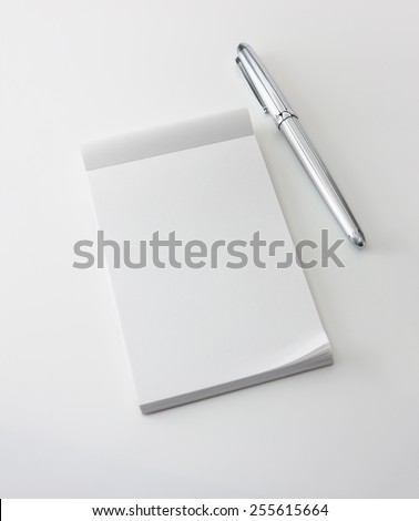 Memo pad and a silver pen, isolated on white with natural shadows. Intentionally highlighted on upper left hand corner. Focus is slightly below memopad top (where messages are likely inserted.)