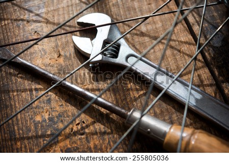 Bicycle repair. A monkey wrench and a screw driver beneath a bicycle wheel spokes. Focus is on wrench turn wheel knob.