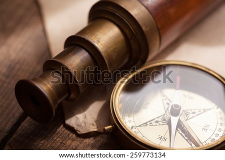 Vintage telescope and compass, on an grungy wood table. Focus is on compass glass and telescope third extension section rim. Shallow depth of field. Intentionally shot with low key shadows.