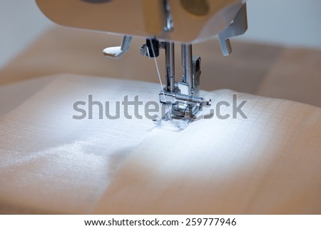 White fabric under a sewing machine, with sewing machine work light illuminating the fabric. Focus is on needle.