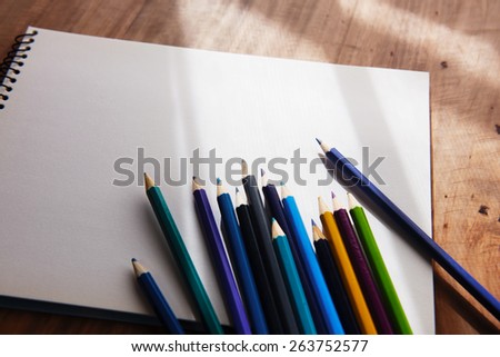 Colored pencils and blank sketch book in by-the-window like light and shadow. Shallow depth of field.