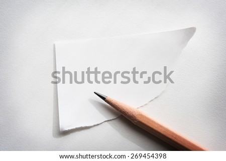 Torn corner piece of memo paper on white desk, with by-the-window type lighting.