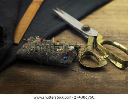 Gold scissors pin cushion, and black fabric.Measuring, cutting, sewing textile or fine cloth. Work table of a tailor. Shallow depth of field, Focus in on  pin on the pin cushion.