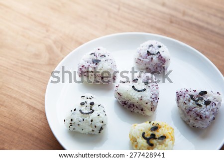 Onigiri rice balls on white plate, with smiley faces made with cut out nori seaweed. Shallow depth of field.