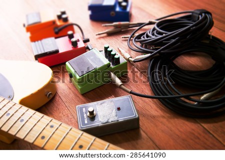 Setting up guitar audio processing effects. Electric guitar and stomp box type effectors and cables on studio floor. Intentionally shot with impressional feel, color and tone.