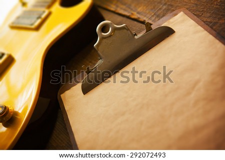 Vintage gold top single cutaway guitar on old wood surface and old clipboard, good for playlists, and production notes. Shallow depth of field.