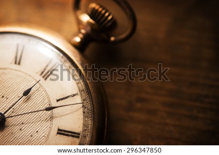 Old pocket watch on grungy wooden desk. Shot in low key and extremely shallow depth for impressional feel. Focus is on etching of clock face plate.