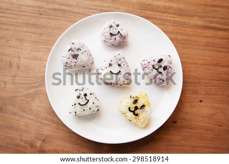 Onigiri rice balls with smiley faces, made with cut out nori seaweed, on white plate.