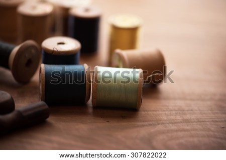 Old sew thread wooden reels or bobbins on a old grungy work table. Tailor's work table. textile or fine cloth making. Shallow depth of field.