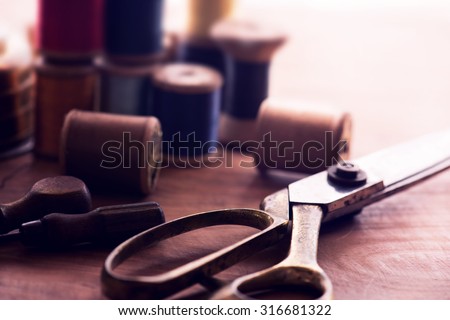 Old sew thread wooden reels or bobbins on a old grungy work table with scissors. Tailor\'s work table. textile or fine cloth making. Shallow depth of field. Intentionally shot in nostalgic muted tone.
