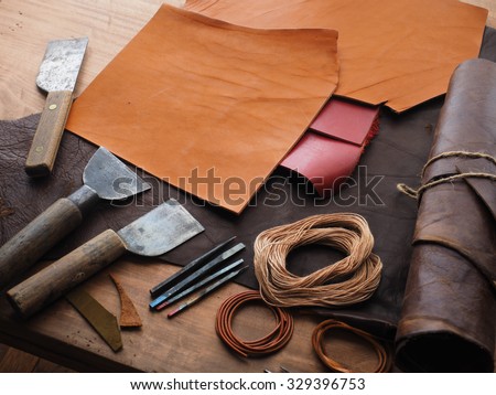 Leathersmith\'s work desk . Pieces of hide and leather working tools on a work table.