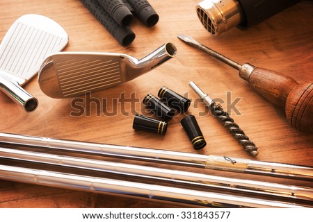 Custom golf clubs or club modifications. Golf club components on a work desk or work bench. grips, shaft, ferrules and, iron head. Focus is on black ferrule parts. Shallow depth of field.