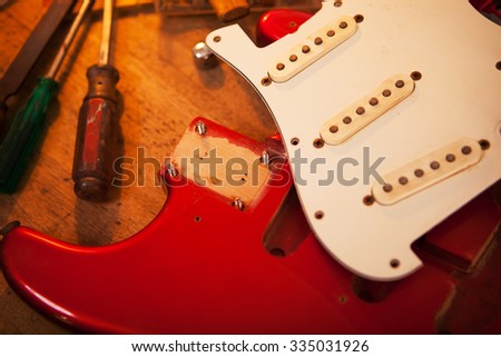 Red electric guitar on guitar repair desk or in a repair work bench. Neck and pickguard detached. Solid body guitar, red metallic color. Shallow depth of field.