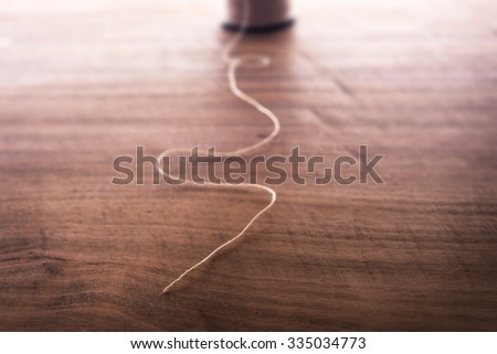Single strand or string end of an spool of thread  for sewing, on rustic wooden work table. Intentionally shot in nostalgic tone. Extremely shallow focus. Focus on string end.